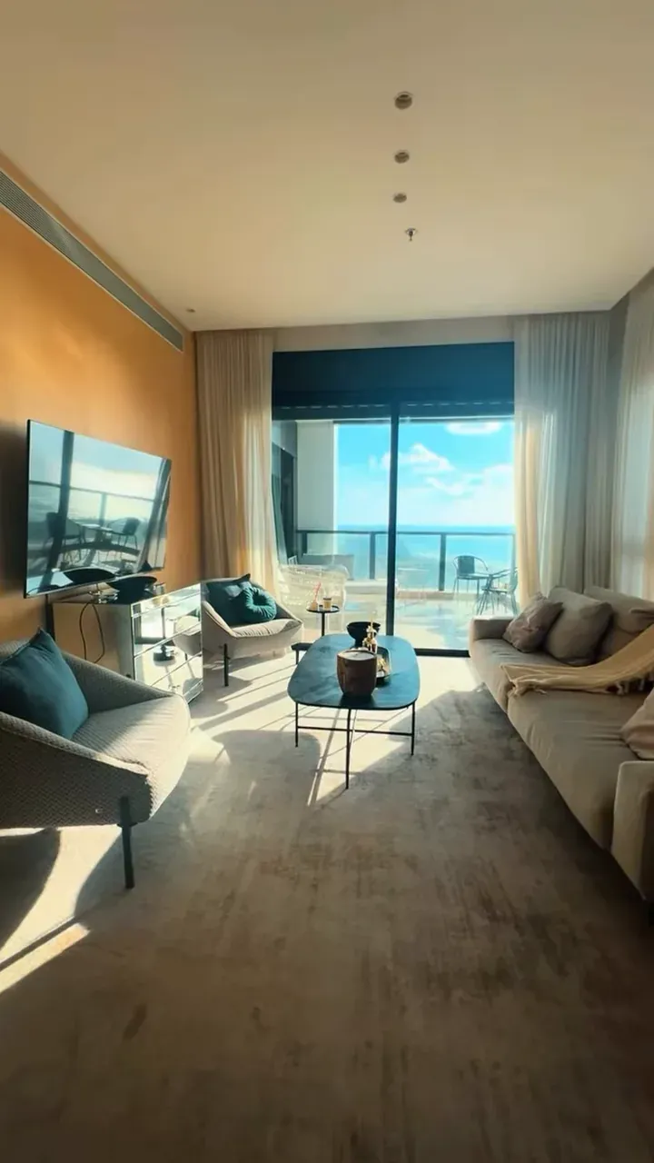 Sala clara com sofás, mesa de centro e porta para a varanda com vista do mar
