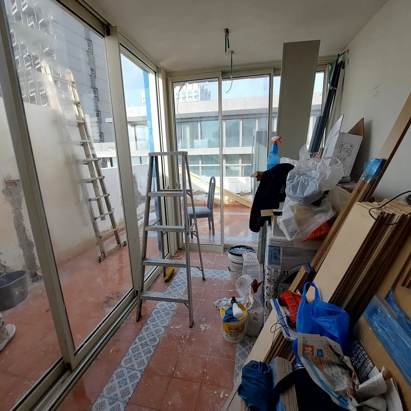 מרפסת סגורה במהלך השיפוץ, עם סולמות, קרשים ושקים של חומרי בניין