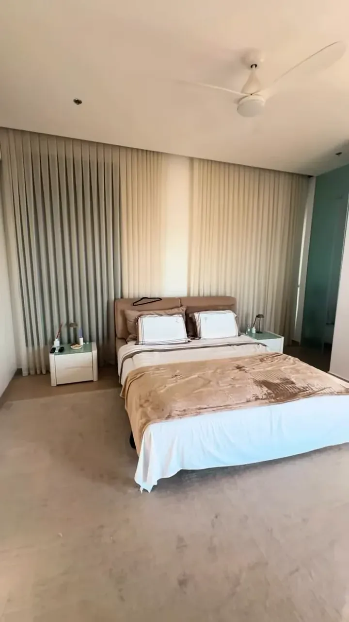 Quarto com cama arrumada, criados-mudos e cortinas longas